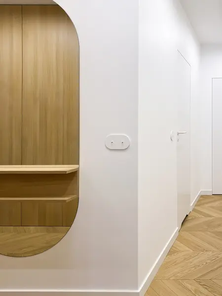 Minimalistyczny przedpokój z drewnianymi akcentami i białymi ścianami.