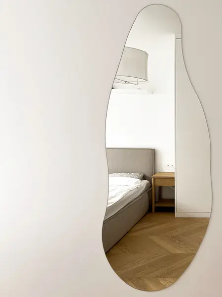 Wnętrze sypialni w stylu minimalistycznym z soft minimalizmem, szare łóżko i lustro.