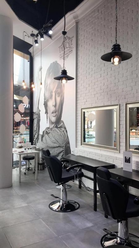 Salon fryzjerski z białymi ścianami, lustrami i stylowymi lampami w stylu glamour.