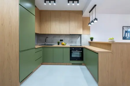 Nowoczesna kuchnia z zielonymi szafkami dolnymi, drewnianymi szafkami górnymi i betonowym backsplash. Jasna przestrzeń w stylu skandynawskim z industrialnymi lampami sufitowymi.