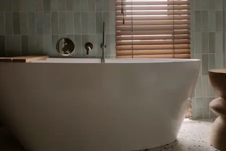 Wnętrze łazienki z białą wanną, zielonymi kafelkami, elementami boho i minimalizmu.