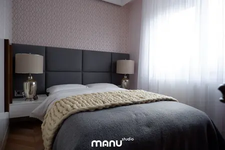Sypialnia z szarym zagłówkiem, białą pościelą i lampą w tradycyjnym stylu.