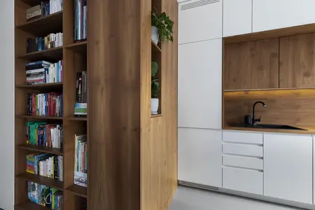 Minimalistyczne wnętrze kuchni z drewnianą półką i nowoczesnymi białymi meblami.
