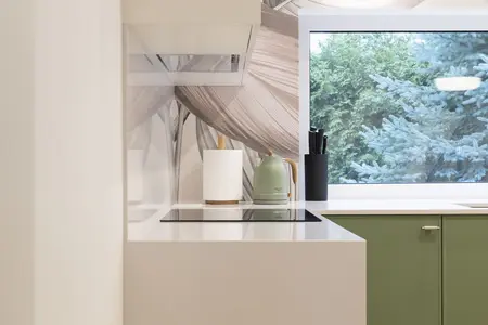 Kuchnia w stylu skandynawskim z zielonymi meblami, białym blatem i nowoczesnym oświetleniem.