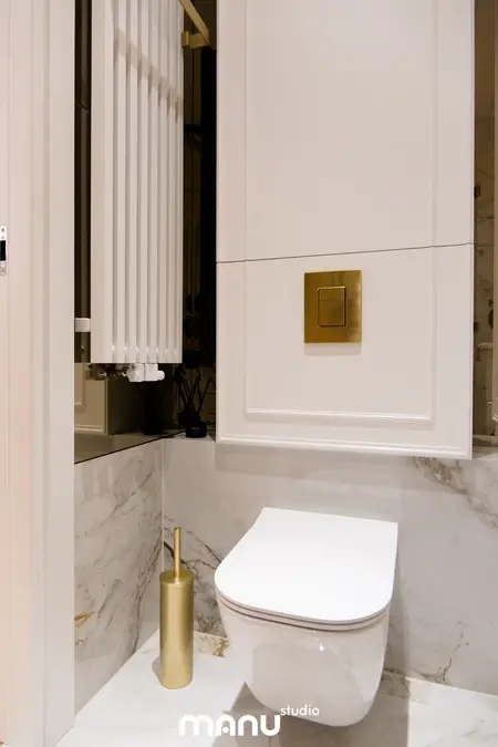 Nowoczesna łazienka z białą toaletą, złotymi detalami i marmurowymi ścianami, styl quiet luxury.
