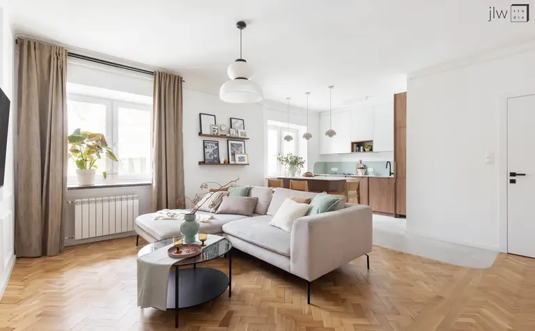 Wnętrze salonu w stylu art deco i skandynawskim z beżową sofą, drewnianym stołem i roślinnością.