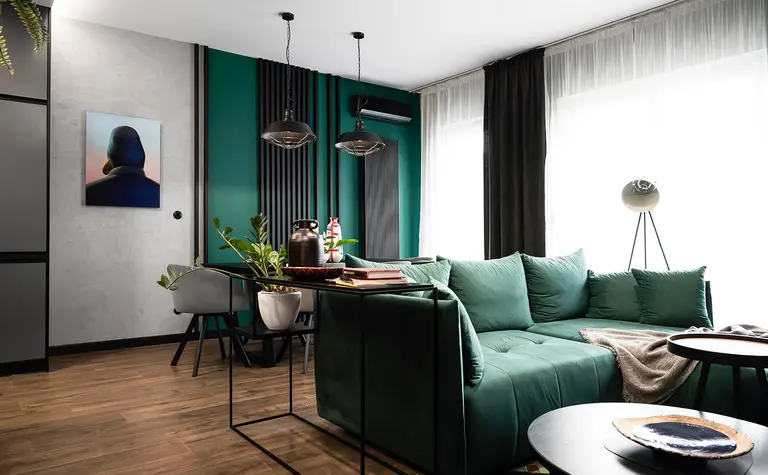 Wnętrze salonu z zieloną sofą, industrialnymi lampami i roślinnymi dekoracjami.