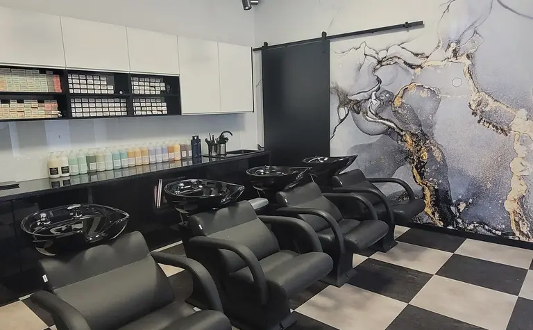 Salon fryzjerski z czarnymi fotelami i nowoczesnym wystrojem.