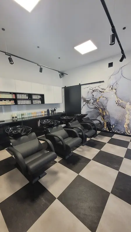 Salon fryzjerski z czarnymi fotelami i nowoczesnym wystrojem.