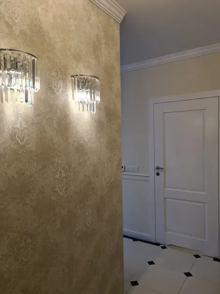 Tradycyjny przedpokój z jasną tapetą i kryształowymi lampami.