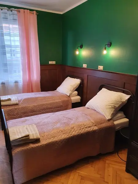 Pokój z dwoma łóżkami, zieloną ścianą i różowymi dodatkami w stylu tradycyjnym i vintage.