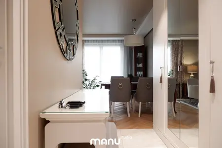 Przestronny przedpokój z lustrem, drewnianą podłogą, roślinami i eleganckimi meblami.