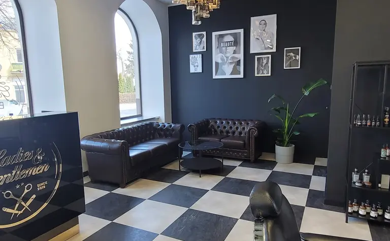 Salon fryzjerski z czarnymi ścianami i białą podłogą w kratę.