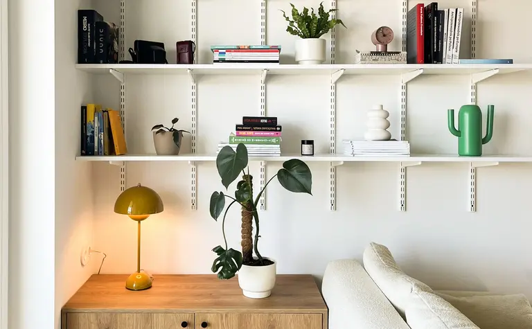 Minimalistyczny salon z drewnianą komodą, białą sofą i roślinami.