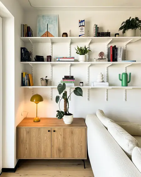 Minimalistyczny salon z drewnianą komodą, białą sofą i roślinami.