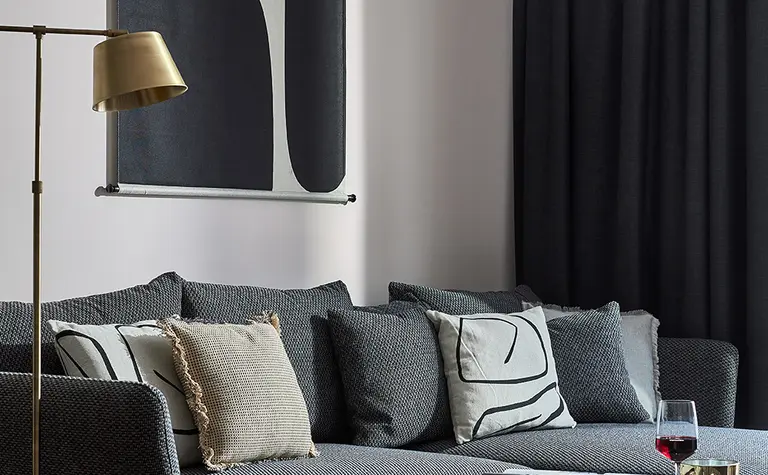 Wnętrze nowoczesnego salonu z szarym sofa, dekoracyjnymi poduszkami i stylowym oświetleniem.
