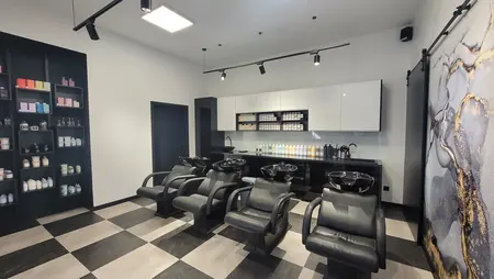 Salon fryzjerski z czarnymi fotelami i kosmetykami na półkach, styl industrialny i nowoczesny.