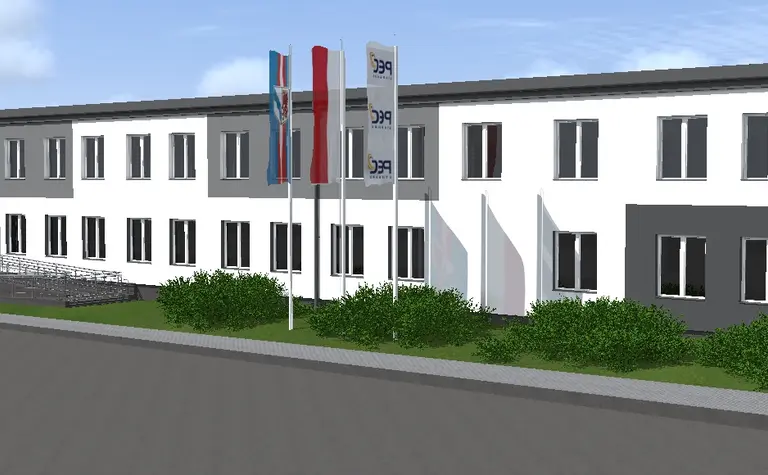Widok budynku z szaro-białą elewacją i zielonymi krzewami, styl industrialny i nowoczesny.