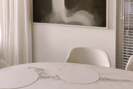 Jadalnia w stylu minimalistycznym z okrągłym stołem, białymi krzesłami i jasnymi zasłonami.