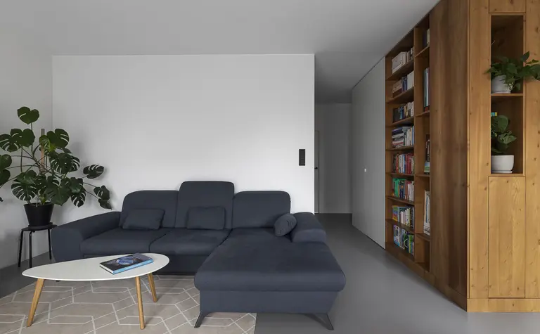 Minimalistyczny salon z niebieską kanapą, drewnianą biblioteczką i rośliną.