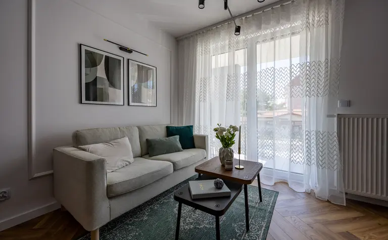 Współczesny salon z jasną sofą, zieloną wykładziną i drewnianymi akcentami.
