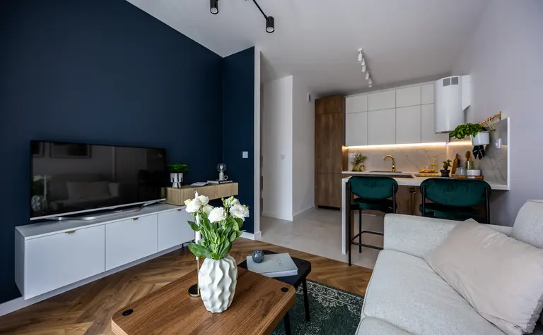 Nowoczesny salon z białymi meblami i drewnianymi detalami, zieloną roślinnością.