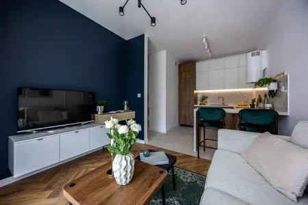 Nowoczesny salon z białymi meblami i drewnianymi detalami, zieloną roślinnością.