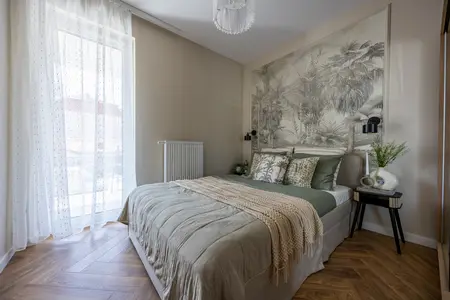 Przytulna sypialnia z dużym łóżkiem w neutralnych odcieniach, ozdobiona tropikalną tapetą nad zagłówkiem, naturalnymi dodatkami i tekstyliami.