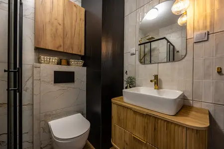Współczesna łazienka z drewnianymi meblami, złotymi detalami i nowoczesną armaturą.