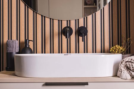 Wnętrze łazienki z białą umywalką i drewnianą ścianą w stylu japandi.