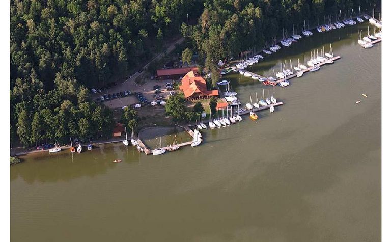 Widok portu z jachtami i drewnianym domkiem otoczonym zielenią. Minimalistyczny i nowoczesny styl.