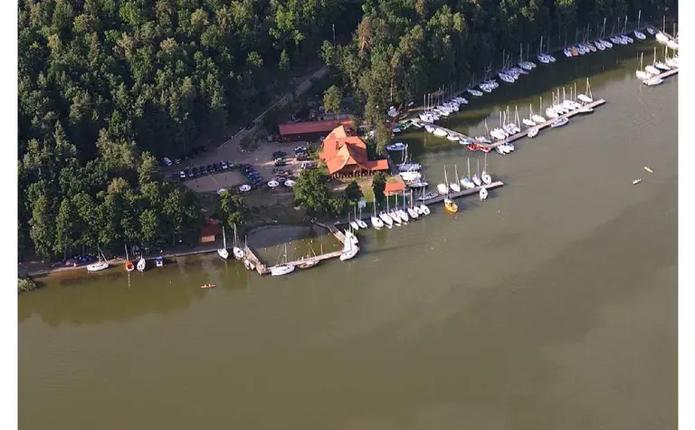 Widok portu z jachtami i drewnianym domkiem otoczonym zielenią. Minimalistyczny i nowoczesny styl.