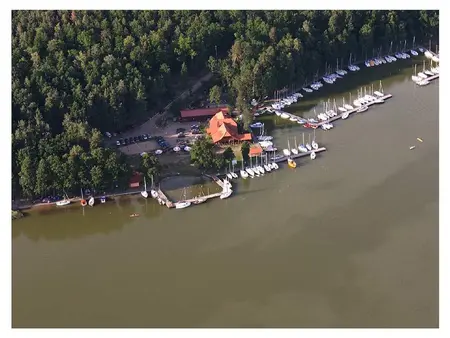 Widok portu z jachtami i drewnianym domkiem otoczonym zielenią. Minimalistyczny i nowoczesny styl.