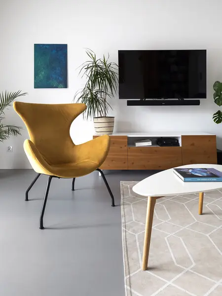 Wnętrze minimalistycznego salonu z żółtym fotelem, telewizorem i roślinami