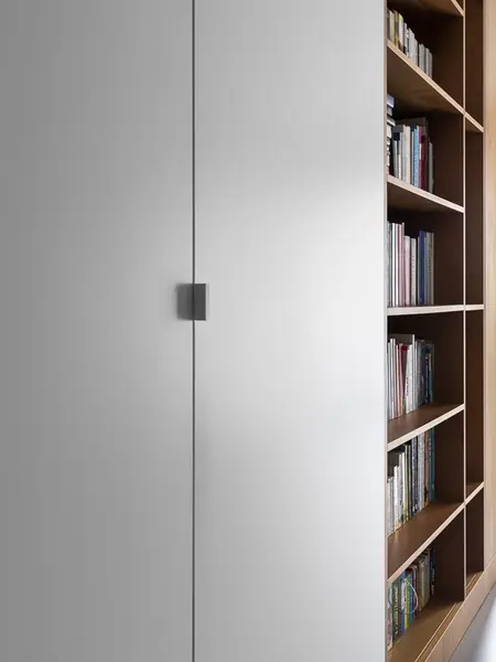 Nowoczesne wnętrze z minimalistyczną białą ścianą i drewnianą półką na książki.