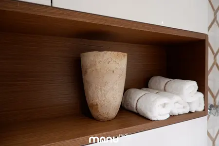 Wnętrze łazienki z drewnianymi półkami, ceramicznym wazonem i białymi ręcznikami.