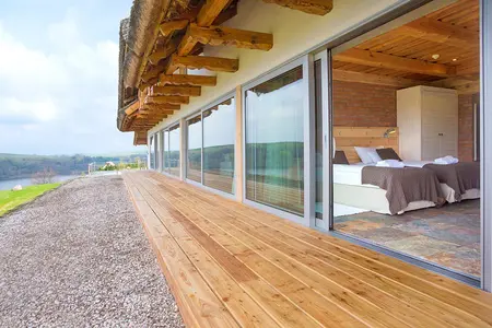 Wnętrze sypialni z minimalistycznym designem, drewnianym tarasem i panoramicznymi oknami.