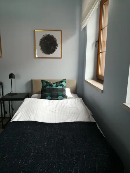 Minimalistyczna sypialnia z łóżkiem, zieloną poduszką i nowoczesnym obrazem.