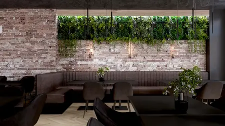 Restauracja z ceglaną ścianą, ciemnymi meblami i roślinnością, styl industrialny.