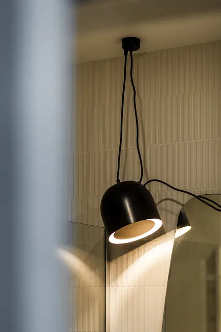 Wnętrze łazienki z lampą w stylu japandi, vintage i współczesnym. Jasne płytki.
