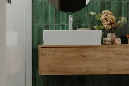 Wnętrze łazienki z zieloną ceramiką i drewnianymi akcentami w stylu skandynawskim.