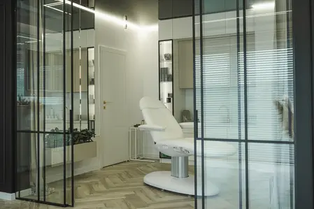Wnętrze gabinetu z białym fotelem, szklanymi ścianami i nowoczesnymi detalami.