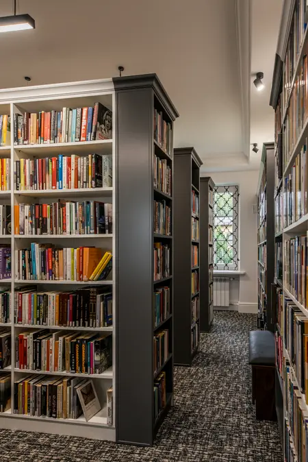 Wnętrze biblioteki z dużymi regałami, tradycyjny styl, książki na półkach, wygodne miejsce do czytania.