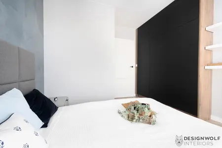 Wnętrze sypialni z szarym tłem, czarną szafą i białą pościelą. Styl industrialny.