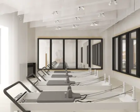 Nowoczesna sala do pilatesu w stylu soft minimalizm z białymi reformerami.