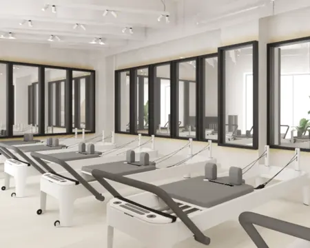 Studio pilates z białymi maszynami i dużymi oknami, soft minimalizm