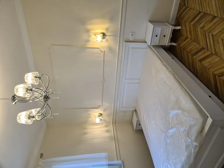 Tradycyjna sypialnia z białym łóżkiem, lustrami i eleganckim oświetleniem.