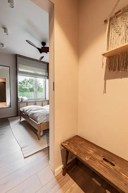 Przedpokój z drewnianą ławką, dużym lustrem oraz jasnymi ścianami. Styl boho, japandi i minimalistyczny.