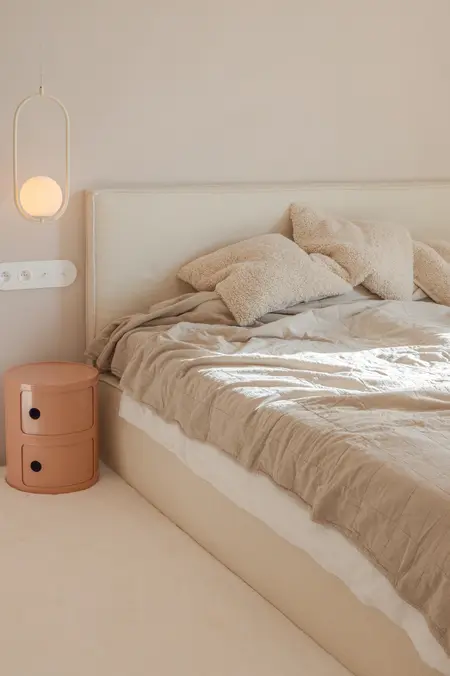 Sypialnia w stylu boho z beżowym łóżkiem, art deco lampą i eklektycznymi dodatkami.