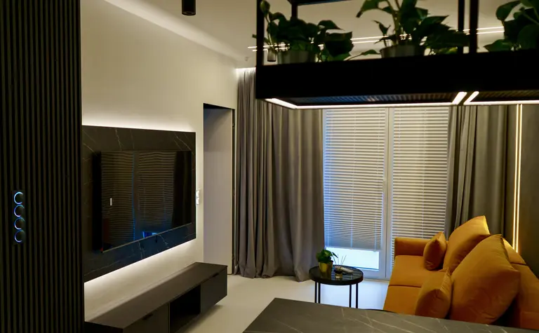 Wnętrze nowoczesnego salonu z szarymi zasłonami, żółtą sofą i stylowym telewizorem.